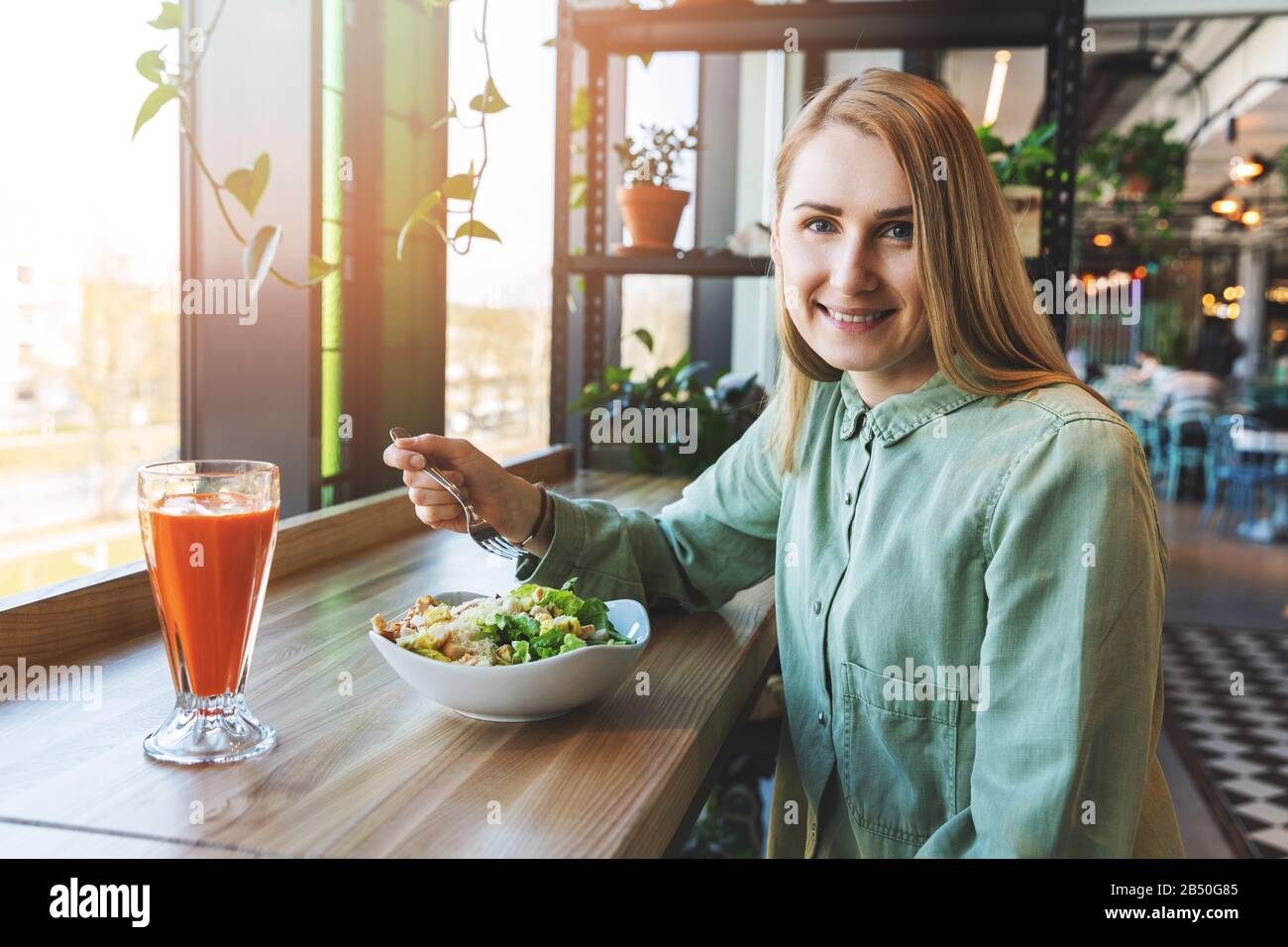 Gesunde Lifestyle-Frau, die im Restaurant zu Mittag gegessen hat. Sie isst unaufhörlichen Salat mit frischem Karottensaft Stockfoto