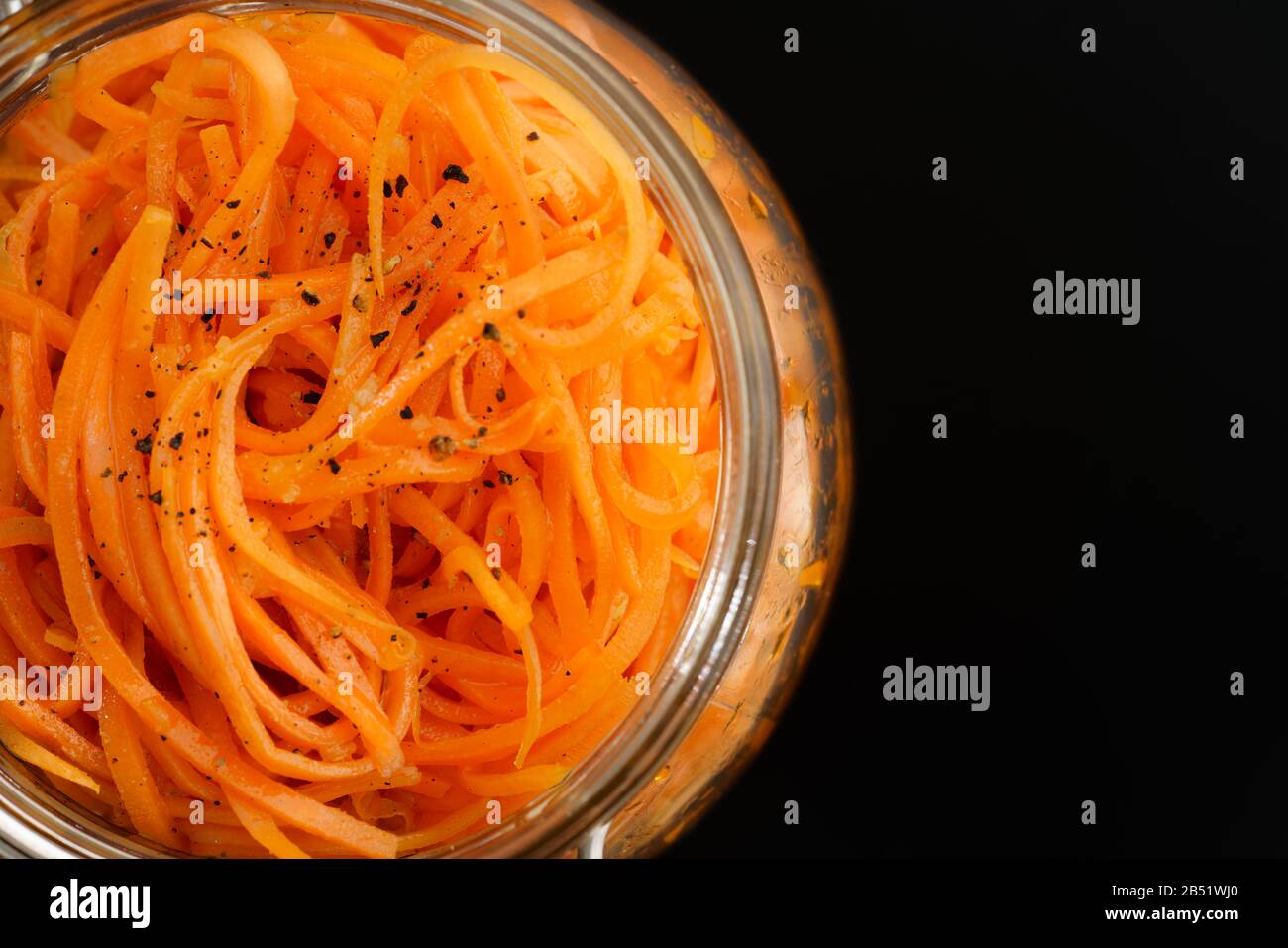 Makroschuss aus würzigem koreanischem Karottensalat mit Öl, Knoblauch und schwarzem Pfeffer. Nachhaltige Verpackung, schwarzer Hintergrund, hohe Auflösung Stockfoto