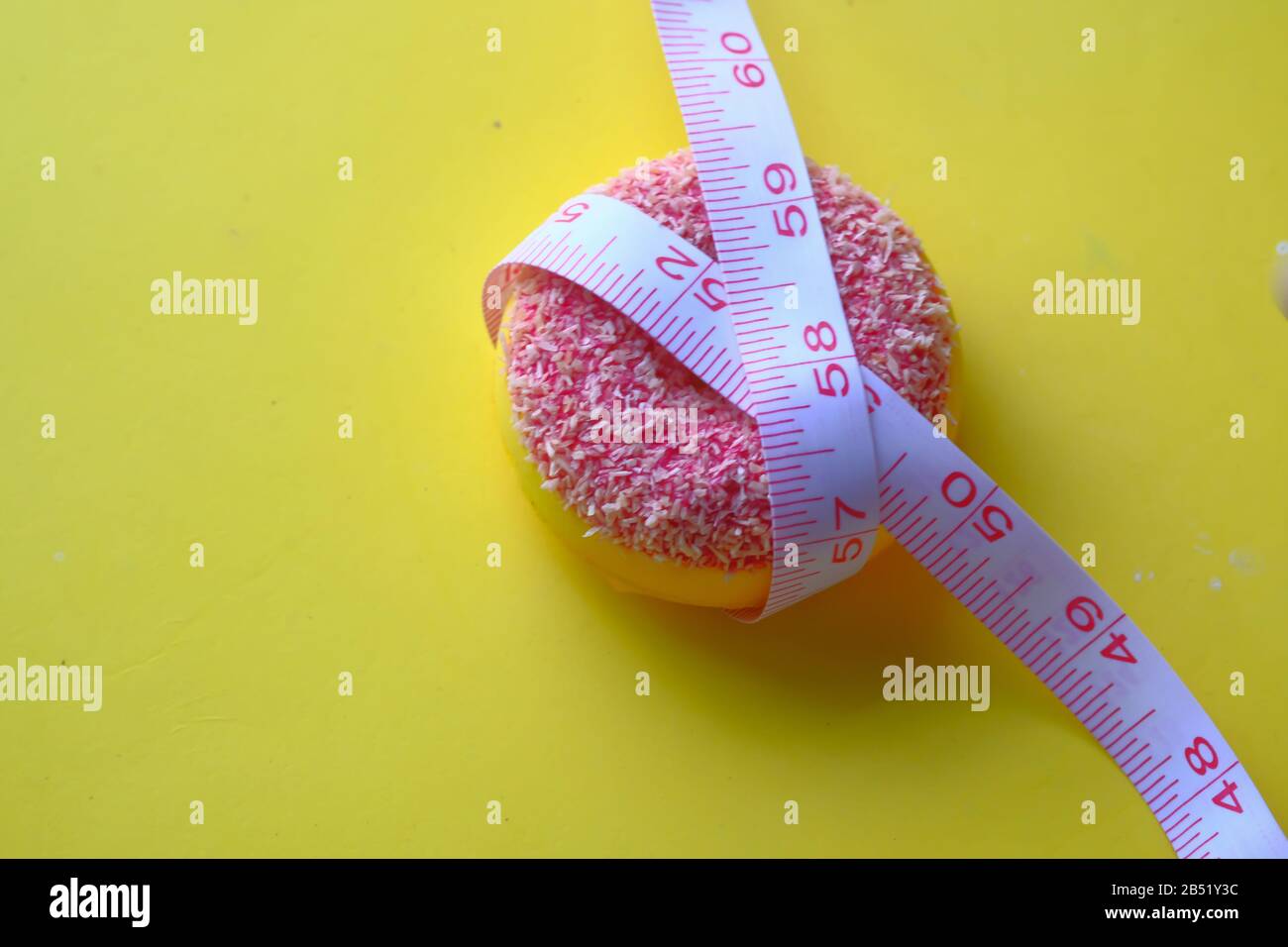 Maßband und bunte Donuts auf gelbem Hintergrund, Nahaufnahme Stockfoto