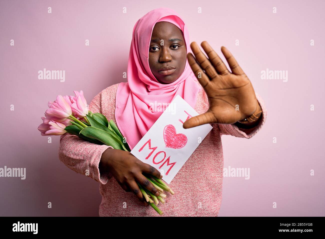 Plus Größe afro-amerikanische Frau, die Hijab mit Nachricht und Tulpen am Muttertag trägt, mit offener Hand, die Stoppschild mit ernsthafter und selbstbewusster Exp macht Stockfoto