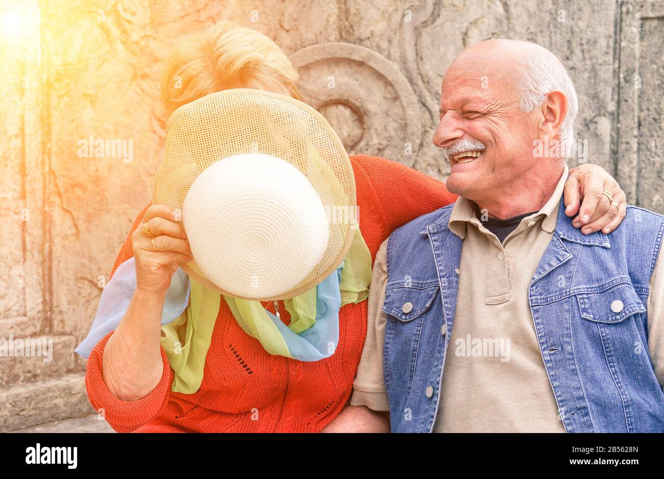 Senioren-Paar hat Spaß, während Frau ihr Gesicht von der Sonne mit Retro-Mode-Hut bedeckt - Fröhlicher älterer aktiver Lebensstil im Old Town City Contest - Lov Stockfoto