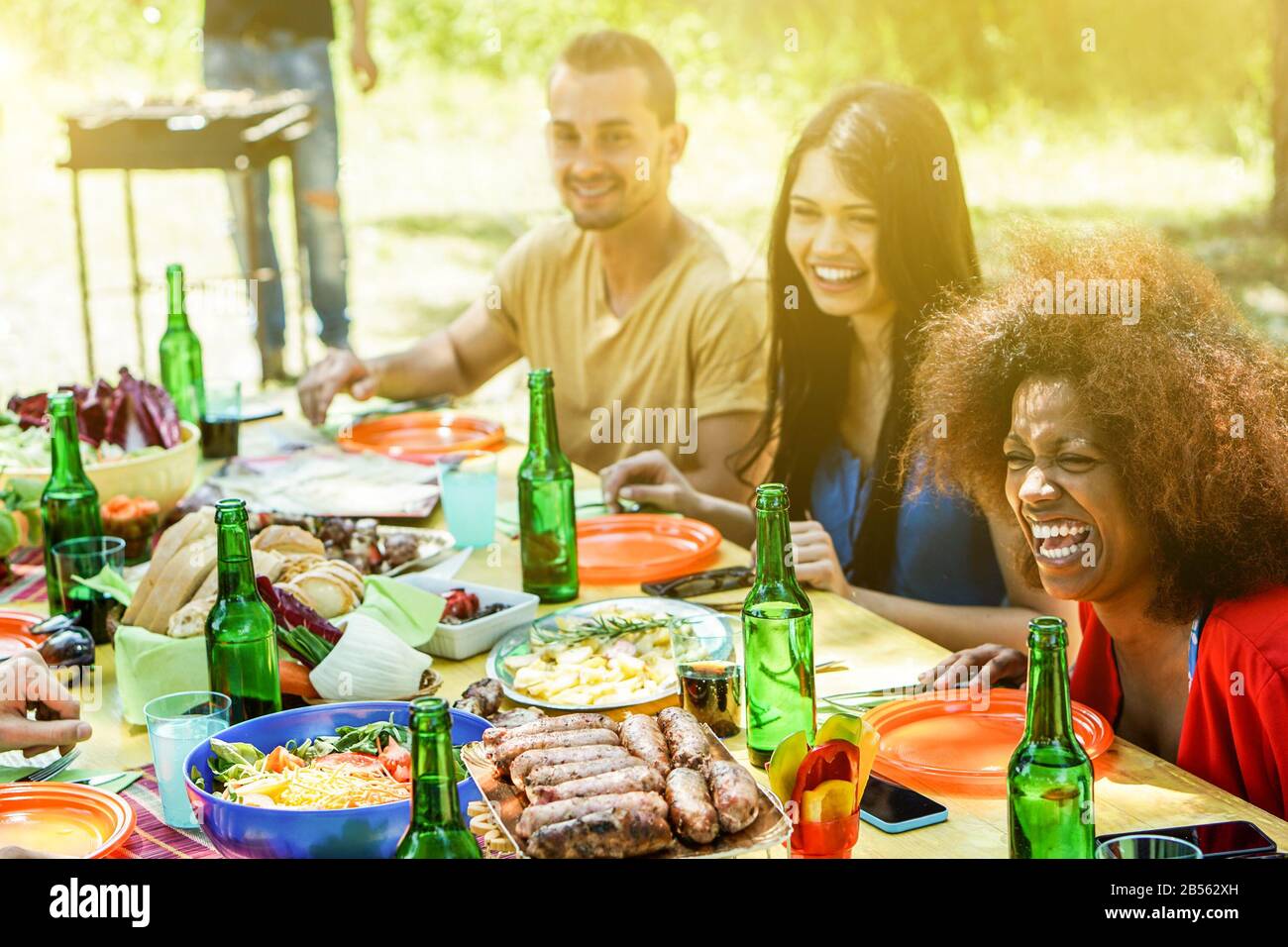 Gruppe verschiedener Kulturschaffende picknick-bbq-Mittagessen im Freien im Garten - Fröhliche Freunde, die Spaß am Grillen haben, Fleisch essen und Bier im Summ toben Stockfoto