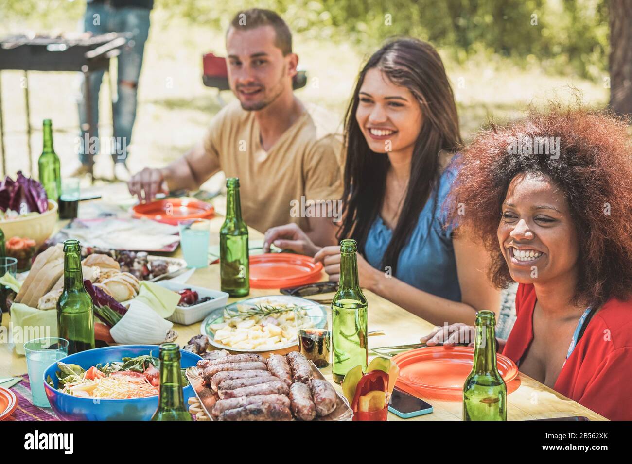 Gruppe glücklicher Leute, die am picknick-grillessen in der Natur lachen - Junge Freunde haben Spaß am Grillen Fleisch essen und Bier trinken im Freien - Konzentrieren Sie Sich auf r Stockfoto