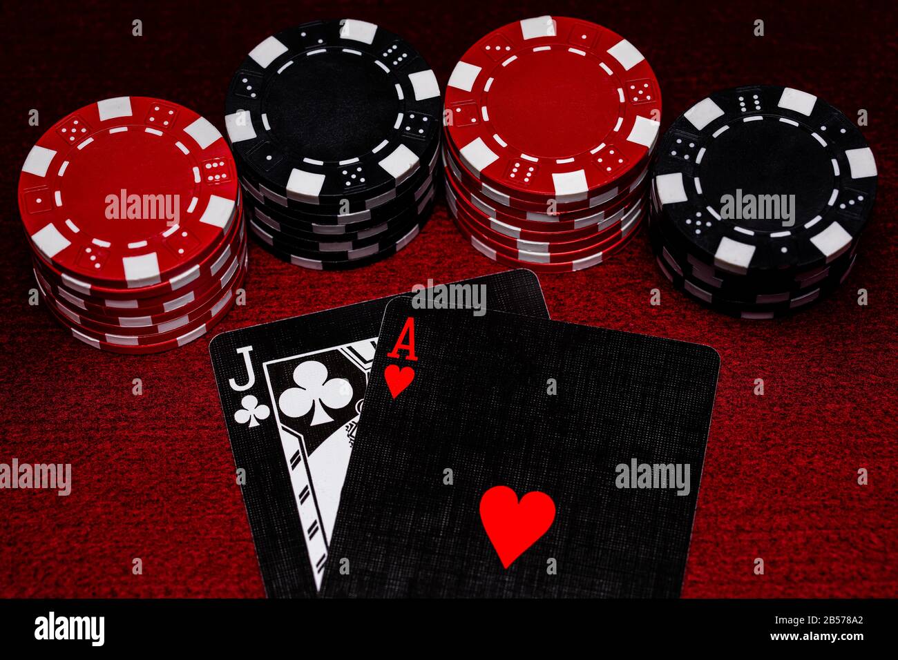 Eine Nahaufnahme der Blackjack Hand mit einzigartigen schwarzen, weißen und roten Karten mit Black and Red Clay Pokerchips auf einer dunkelroten Filztischoberfläche. Platz für Co Stockfoto