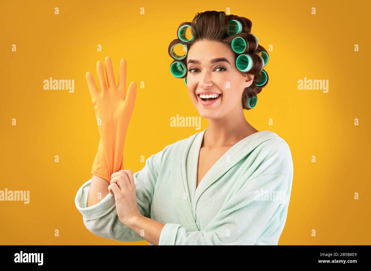 Glückliche Hausfrau, Die Handschuhe Aufsetzt, Die Über Yellow Studio Hintergrund Posieren Stockfoto