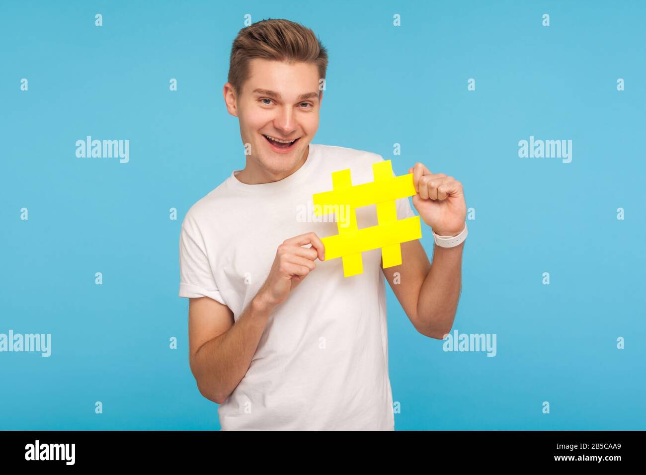 Beliebte Inhalte. Fröhlicher lustiger Mann in weißem T-Shirt mit großem gelben Hashtag-Symbol und lächelnd, Hash-Zeichen von Internettrends, viralen Social Media-topi Stockfoto