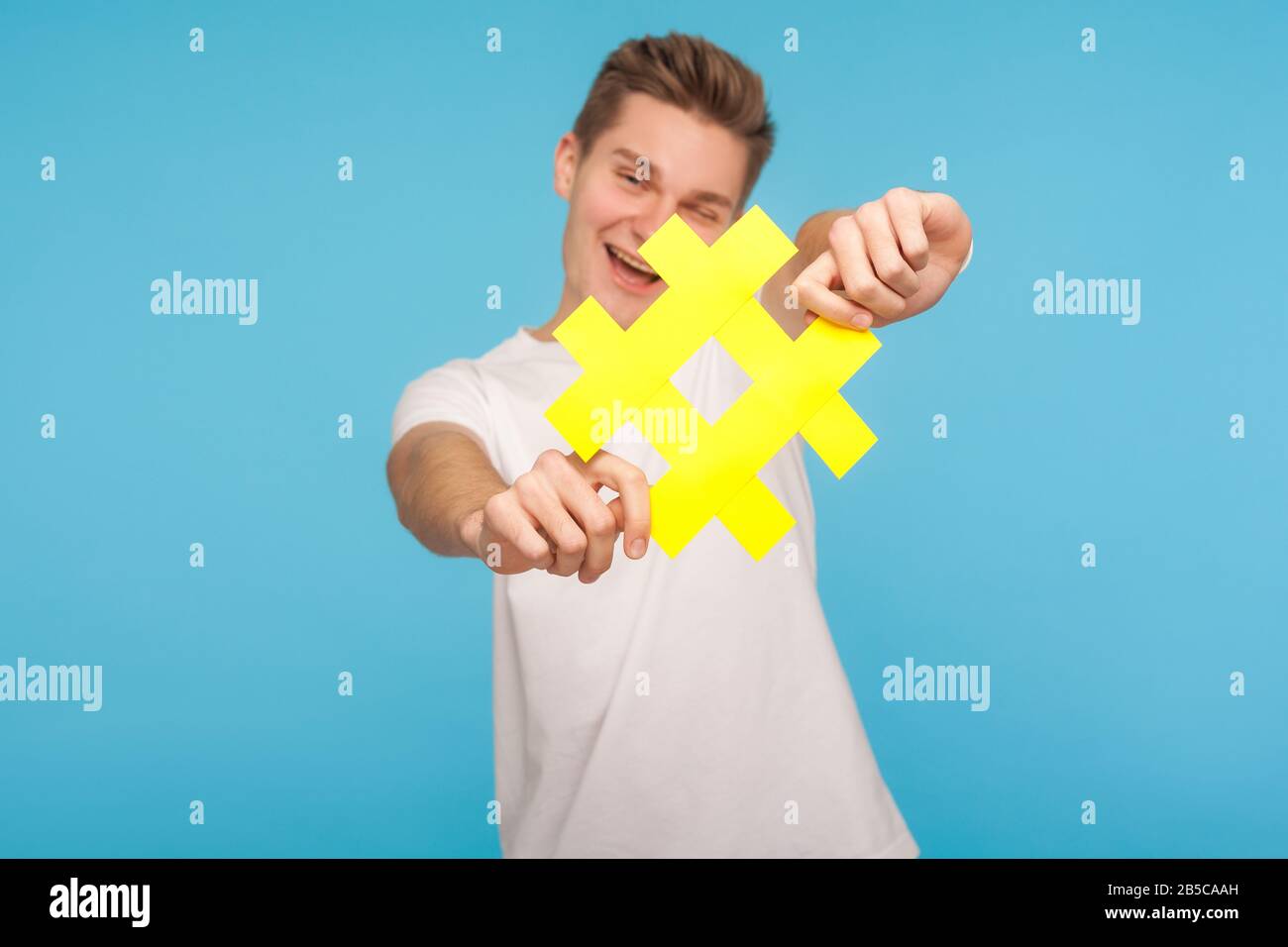 Folgen Sie dem trendigen Blog. Fröhlicher Mann im T-Shirt, der das gelbe Hashtag-Symbol an die Kamera hält, Hash-Zeichen zeigt und virale Social-Media-Topi empfiehlt Stockfoto