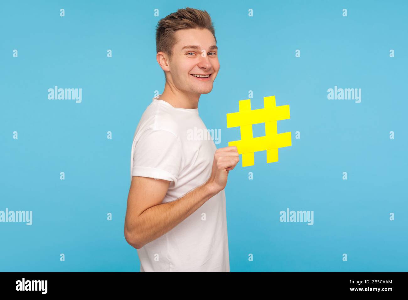 Internettrends. Profil des fröhlichen lustigen Mannes im T-Shirt mit großem gelben Hashtag-Symbol und lächelnd, mit Hash-Zeichen für virales Social Media-Thema. I Stockfoto