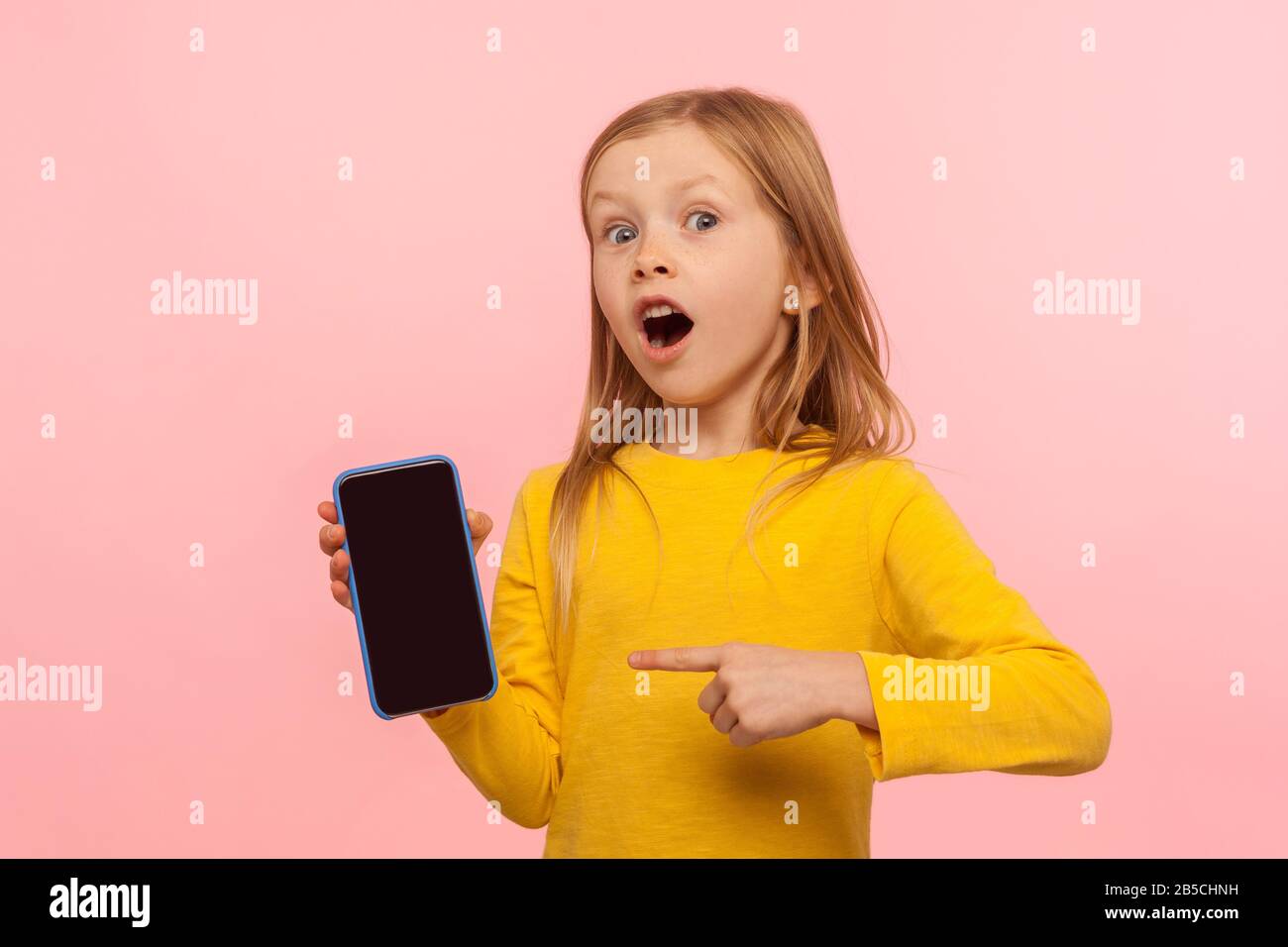 Wow, sehen Sie sich das Handy an! Stauntes kleines Mädchen, das Telefon zeigt und die Kamera mit überraschtem schockierten Gesicht, Werbung für Mobilgeräte, Kinderservice ansieht Stockfoto