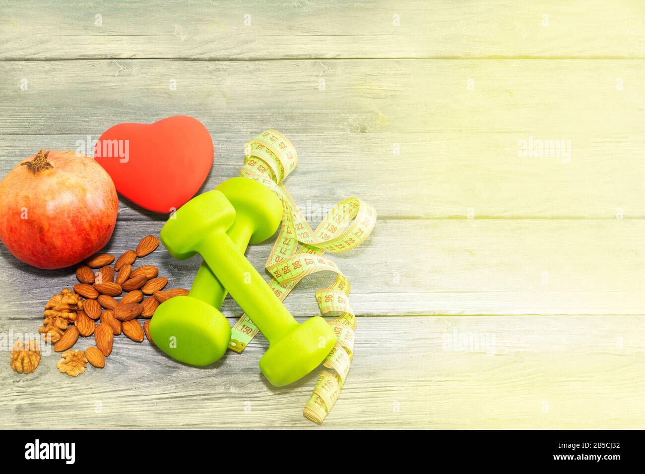 Granatapfelfrucht, Kurzhanteln, Nüsse auf Holzhintergrund. Das Konzept der Gesundheit, gesundes Herz. Stockfoto