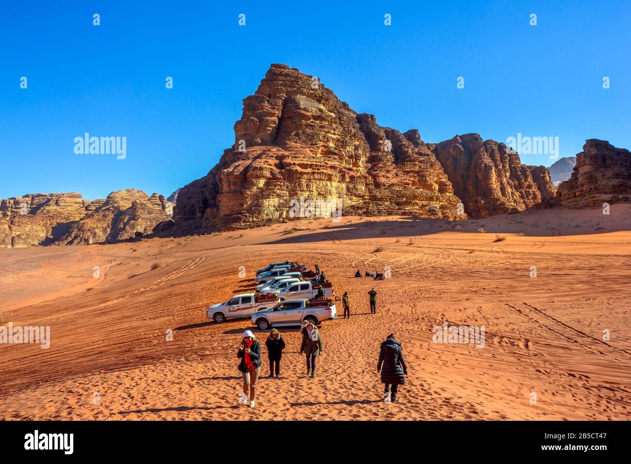 Aqaba, Jordanien - 5. Januar 2020: Geländewagen, die auf Touristen warten, die von Felsen auf den roten Dünen der Wüste Wadi Rum, Tal des Mondes, a Stockfoto