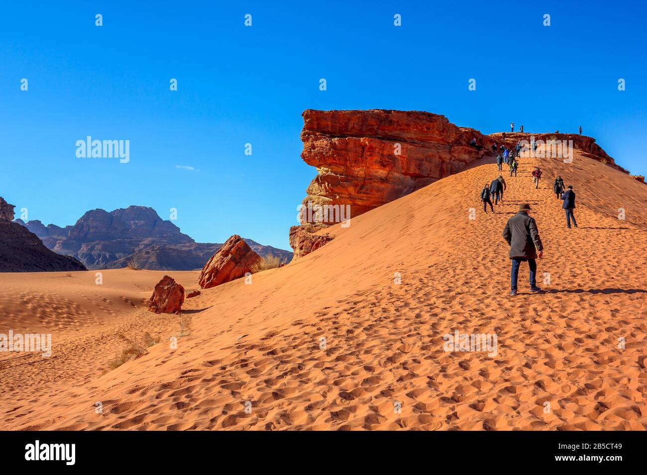 Aqaba, Jordanien - 5. Januar 2020: Die Menschen erklimmen die Dünen in der Wüste Wadi Rum am Gipfel des roten Felsens. Das Tal des Mondes ist ein beliebtes Touristenziel Stockfoto