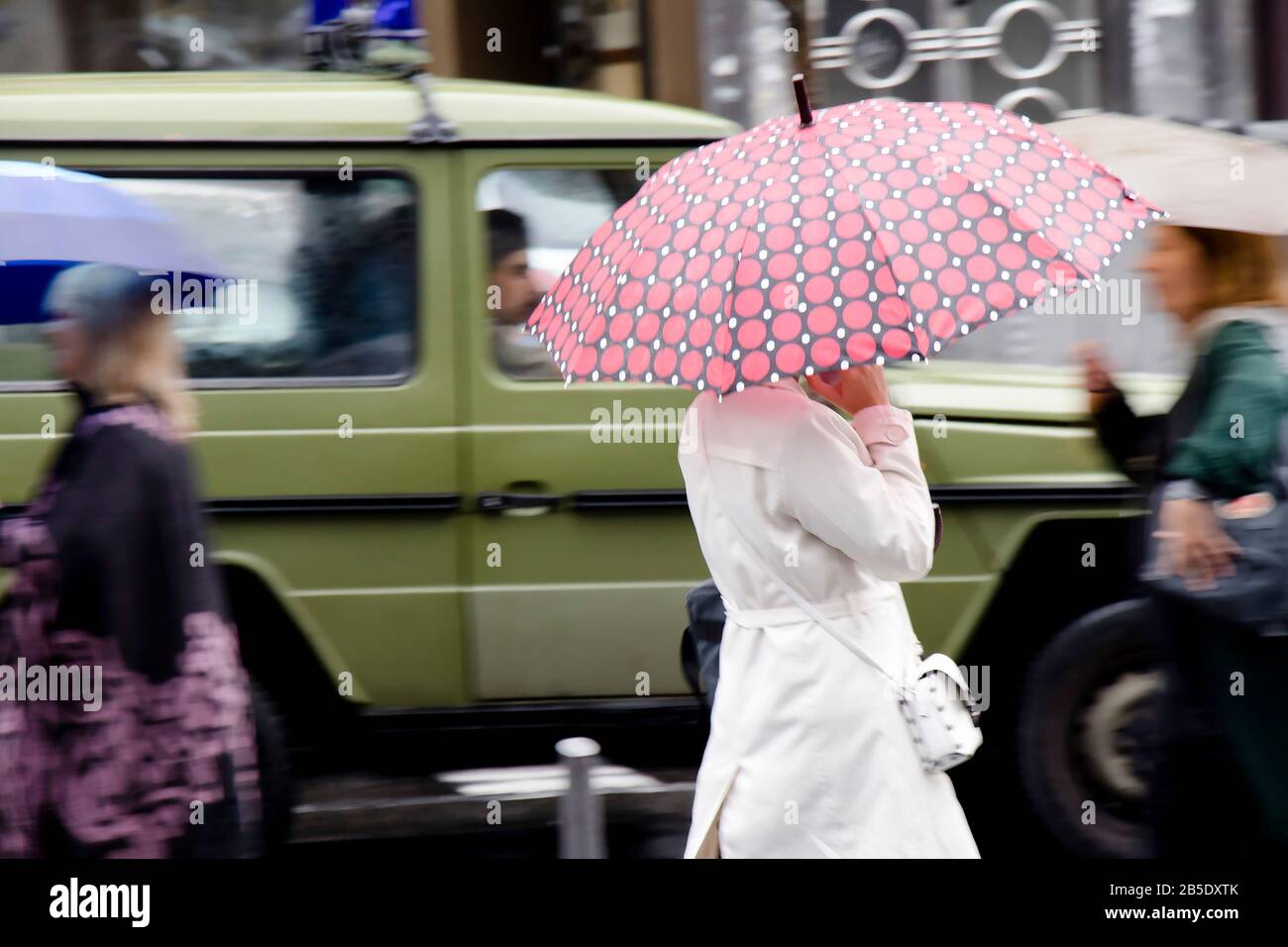 Belgrad, Serbien - 24. September 2019: Junge Frau in weißem Regenmantel, die an einem geschäftigen Tag in Bewegung unter dem Regenschirm auf einer regnerischen Stadtstraße spazieren geht Stockfoto