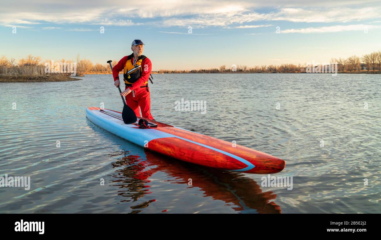 Senioren-Paddler in einem Trockenanzug und einer Schwimmweste paddeln auf einem See in Colorado, im Winter oder im Frühjahr auf einem langen Rennstativ auf. Stockfoto