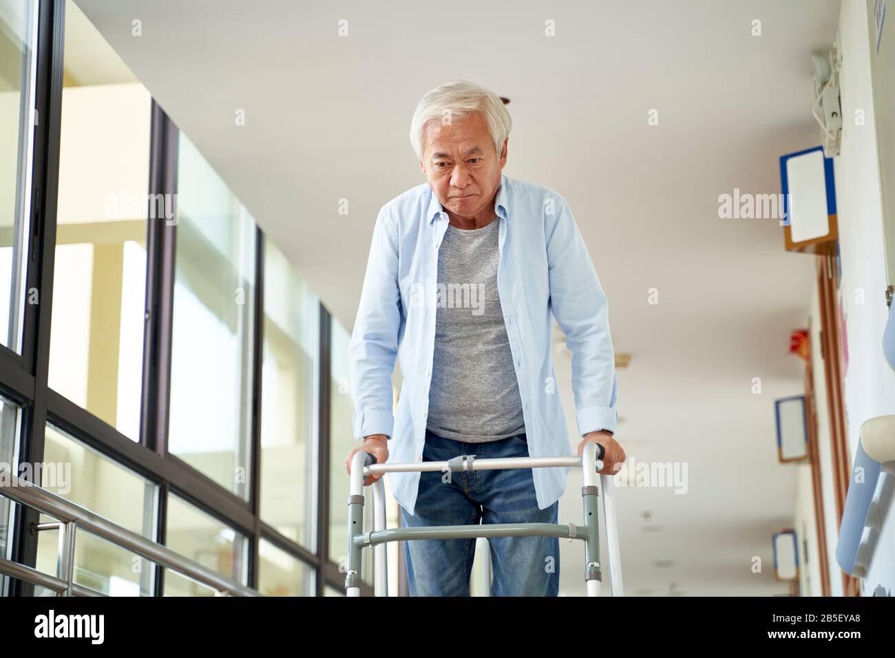 asiatischer Mann, der mit einem Geher im Flur des Krankenhauses oder Pflegeheims spazieren ging Stockfoto