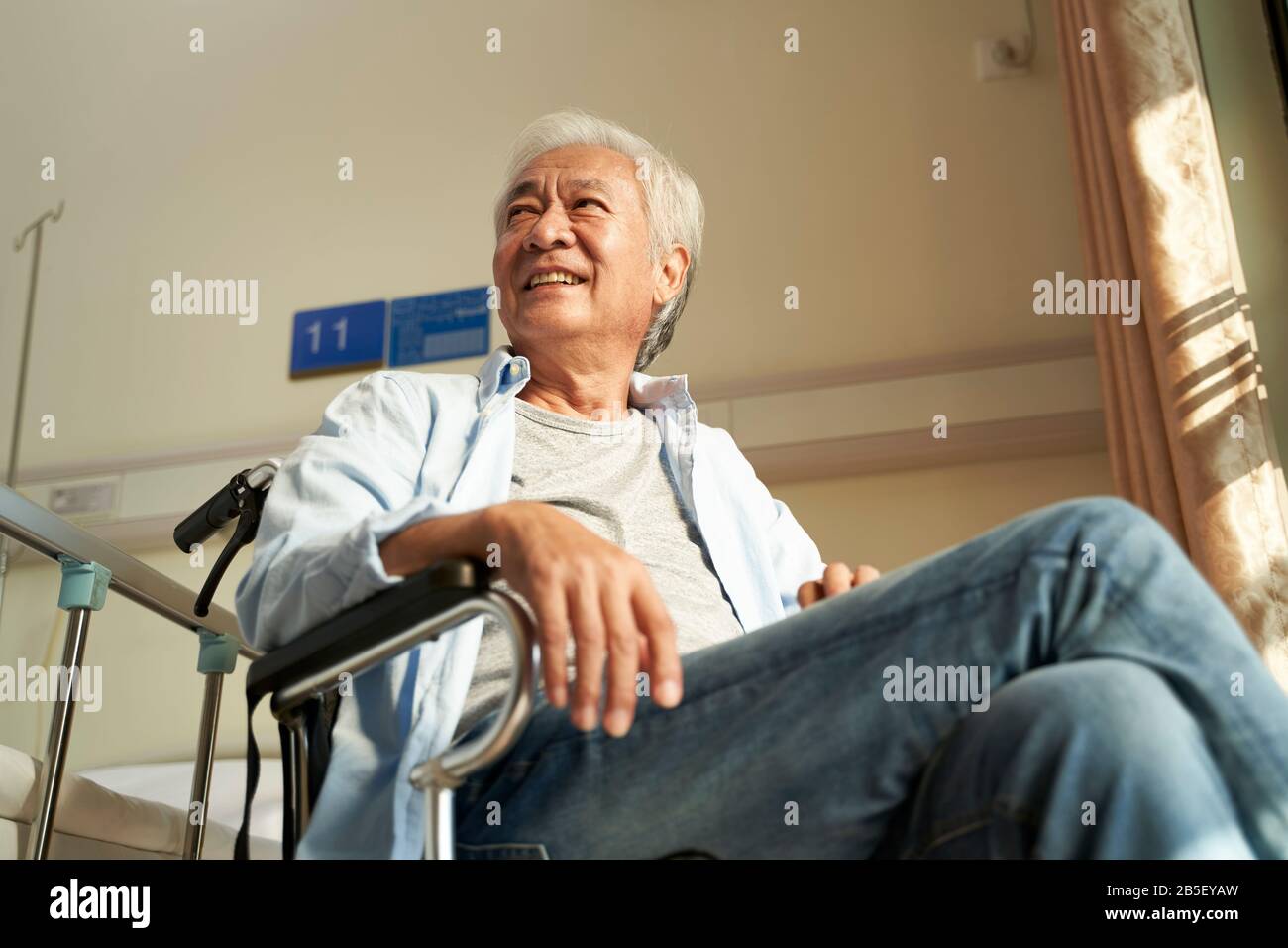Asiatischer alter Mann sitzt im Rollstuhl im Pflegeheim oder in der Krankenstation und sieht glücklich und zufrieden aus Stockfoto