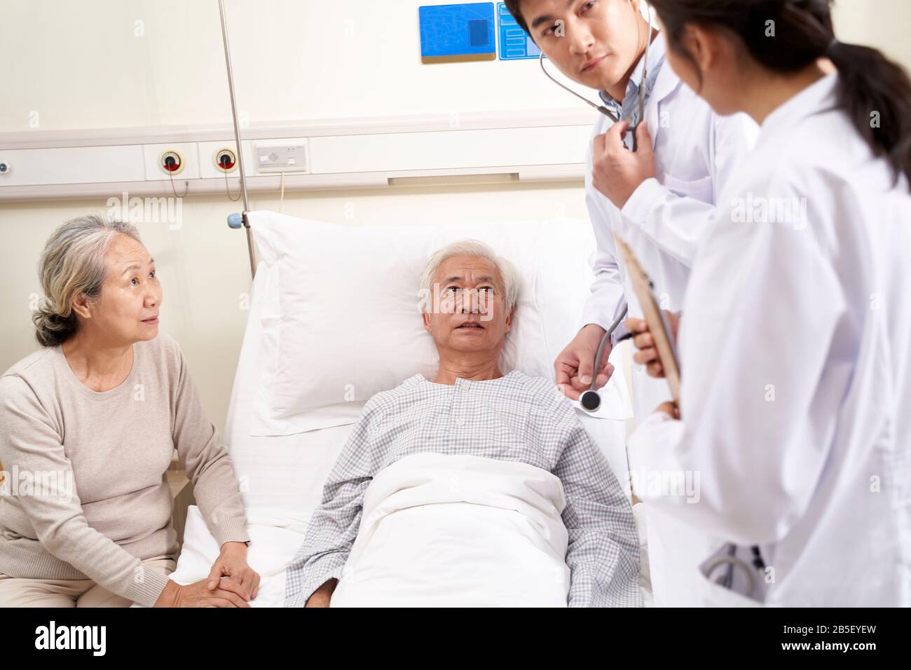 Junger asiatischer Arzt untersucht älteren Patienten, der über seinen medizinischen Zustand in der Krankenstation spricht Stockfoto
