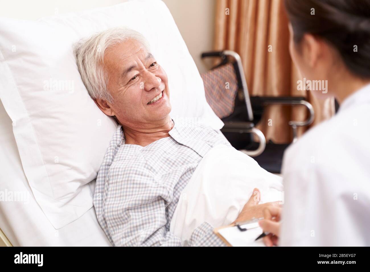 Jungen asiatischen Arzt im Gespräch mit älteren Patienten am Krankenbett in hosptial Ward Stockfoto