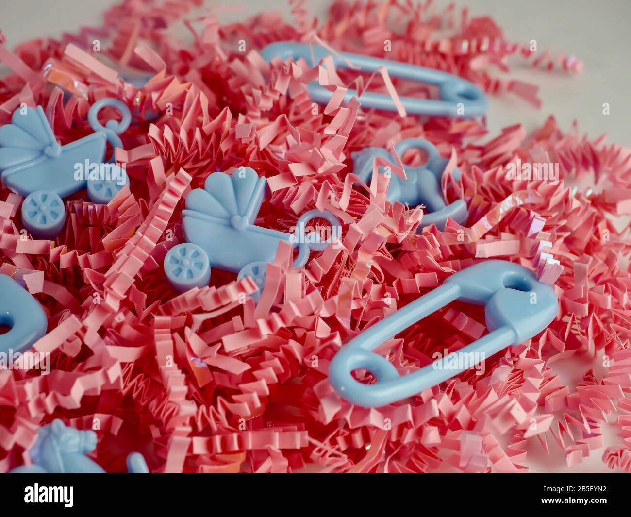 Baby Junge oder Baby Mädchen, pinkfarbener Papierschrot mit blauen Sicherheitsnadeln, Kinderwagen und Schaukelpferden für eine Babydusche oder ein Geschlecht enthüllen Party. Stockfoto