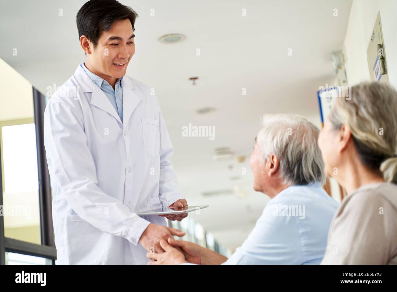 Freundlicher junger asiatischer Arzt, der im Wartebereich mit älteren Patienten im Krankenhaus die Hände schüttelt Stockfoto