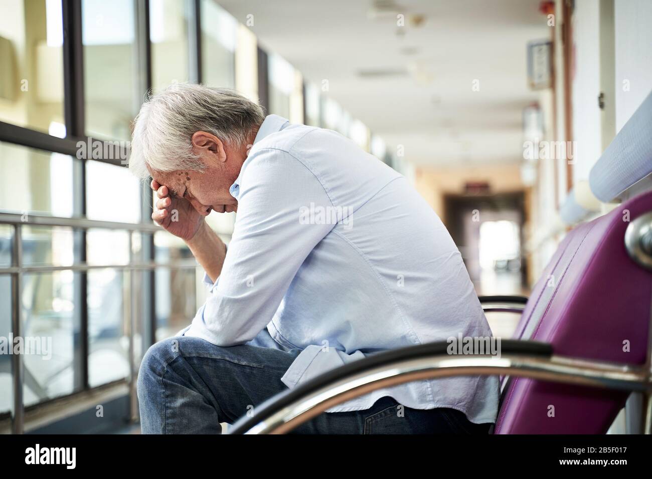Asiatischer alter Mann, der auf dem Flur des Krankenhauses sitzt, sieht traurig und depressiv aus Stockfoto