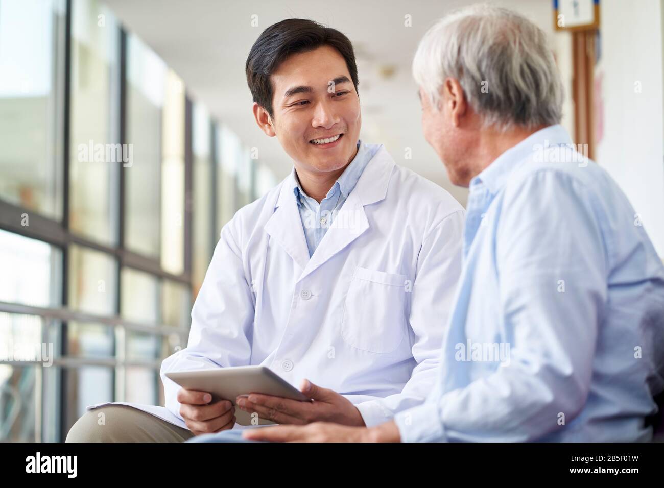 Freundlich lächelnder junger asiatischer Arzt, der das Testergebnis für ältere Patienten im Krankenhaus spricht und erklärt Stockfoto
