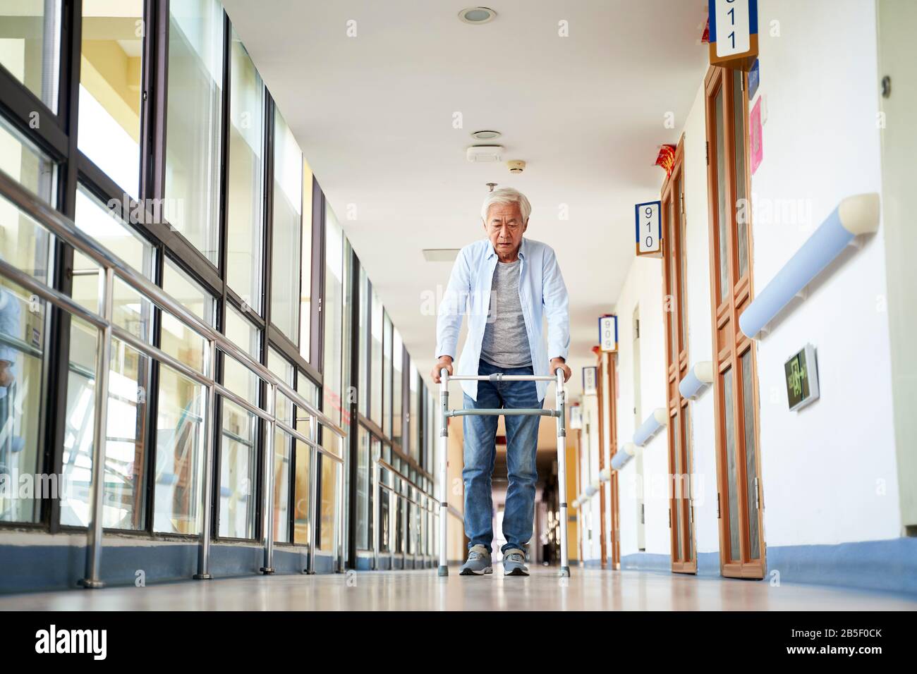 Leitender asiat, der mit einem Geher im Flur des Pflegeheims spazieren ging Stockfoto