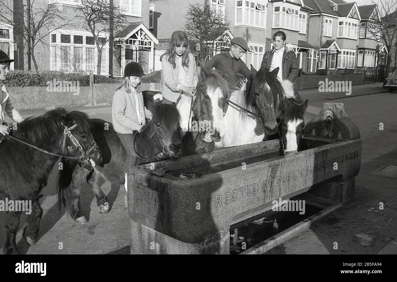 In den 1970er Jahren, historisch, halten Jugendliche auf Pferden und Ponys in einer ehemaligen Wasserrinne aus Stein, die im Jahre 1888 errichtet wurde, um ihren Tieren während eines heißen Sommers Erfrischung zu geben, South London, England. Im Laufe des Jahrzehnts waren einige der Sommer extrem heiß. Stockfoto