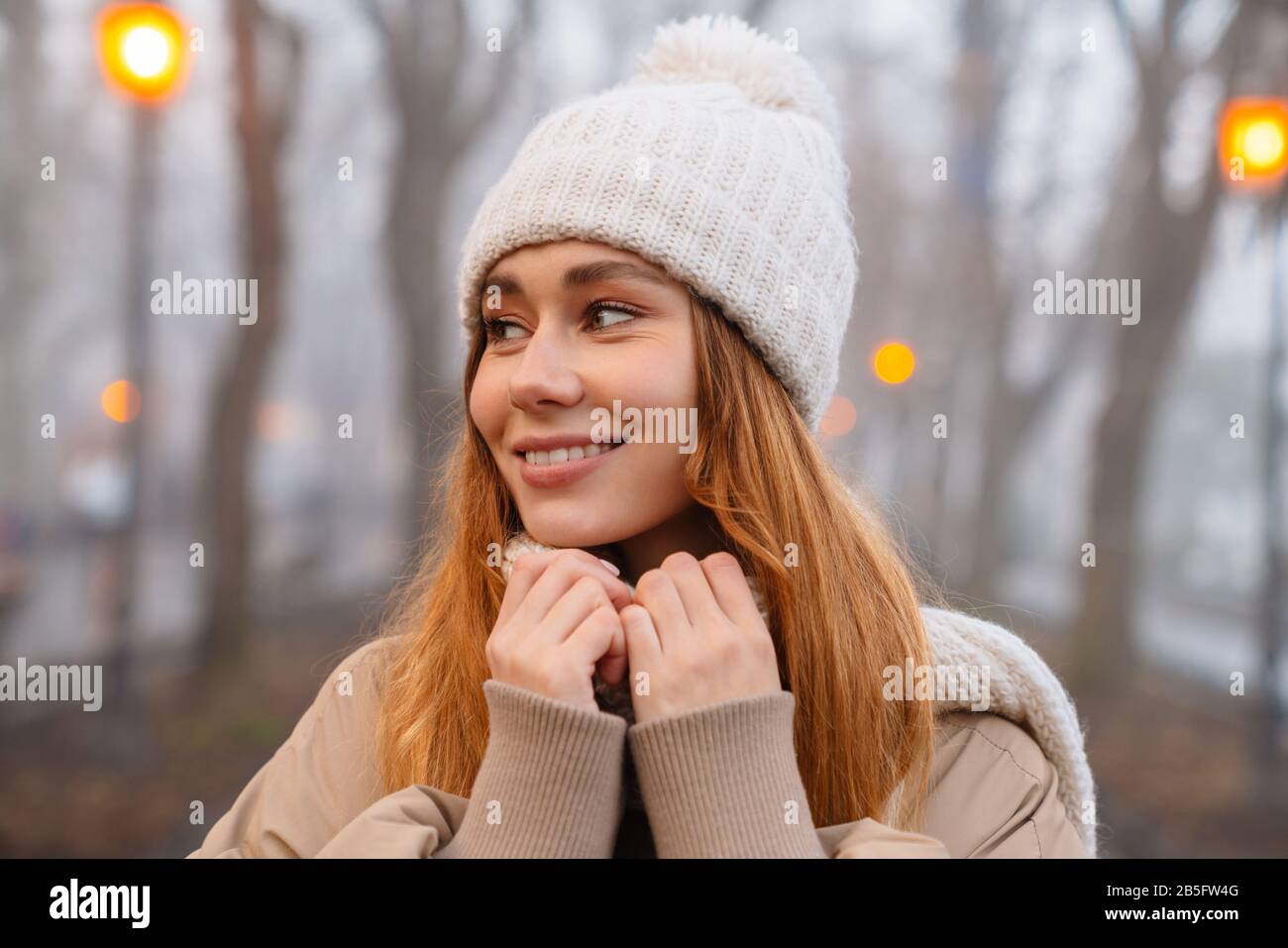 Attraktives lächelndes junges Mädchen, das am Abend Winterkleidung im Park trägt Stockfoto