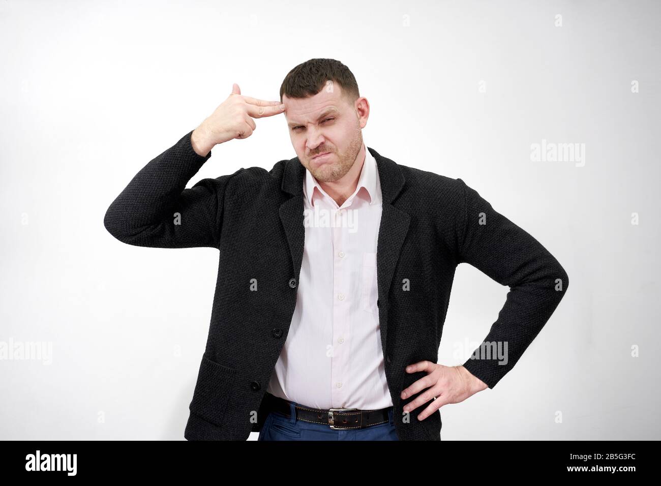 Der Mann zeigt mit dem Finger auf den Kopf, um sich auf einem grauen Hintergrund, einem Stresskonzept, zu schießen Stockfoto