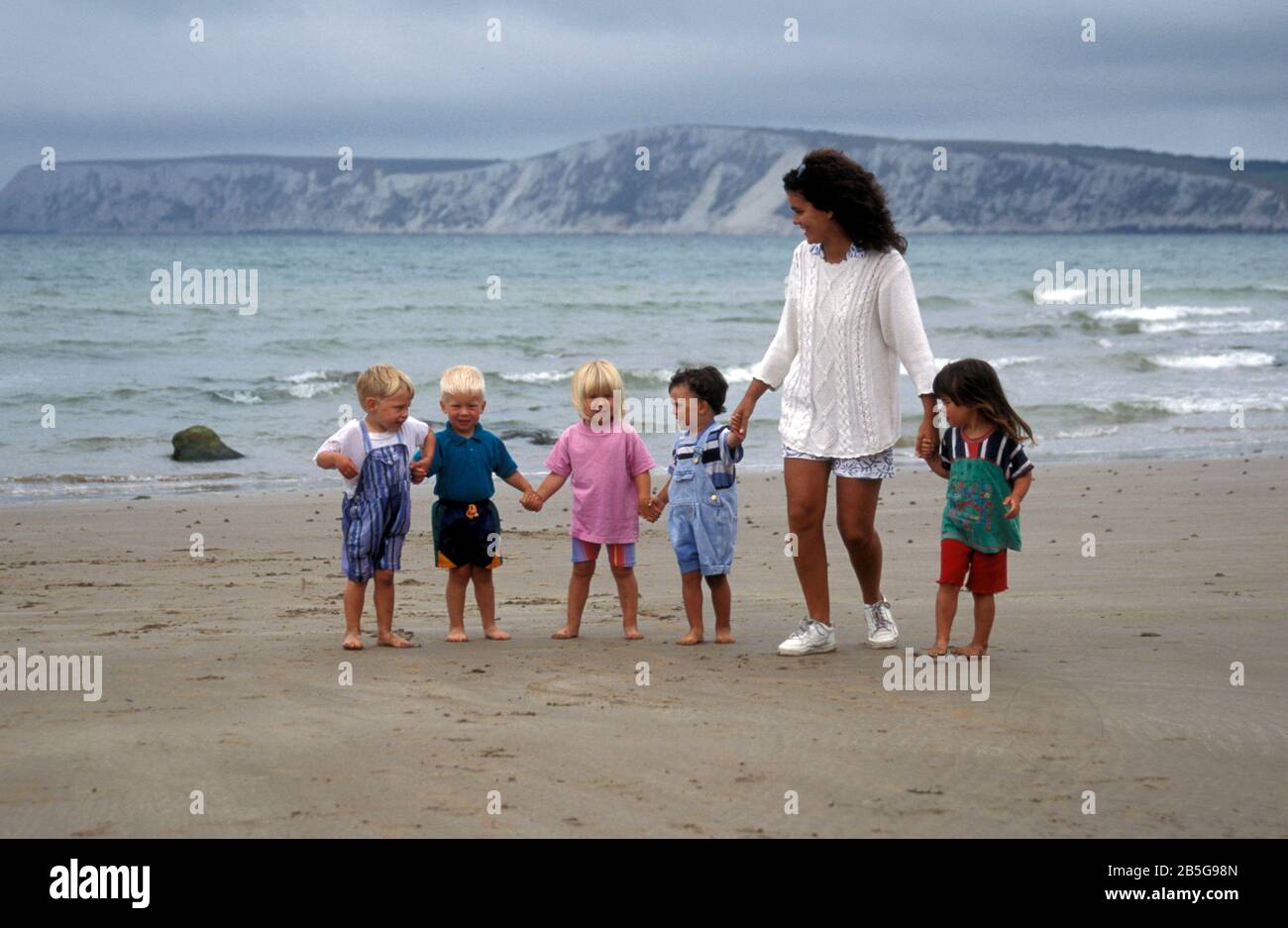 Frau, die mit 5 Kleinkindern am übergiebelten Tag am Strand spazieren geht, Insel Wight, England Stockfoto