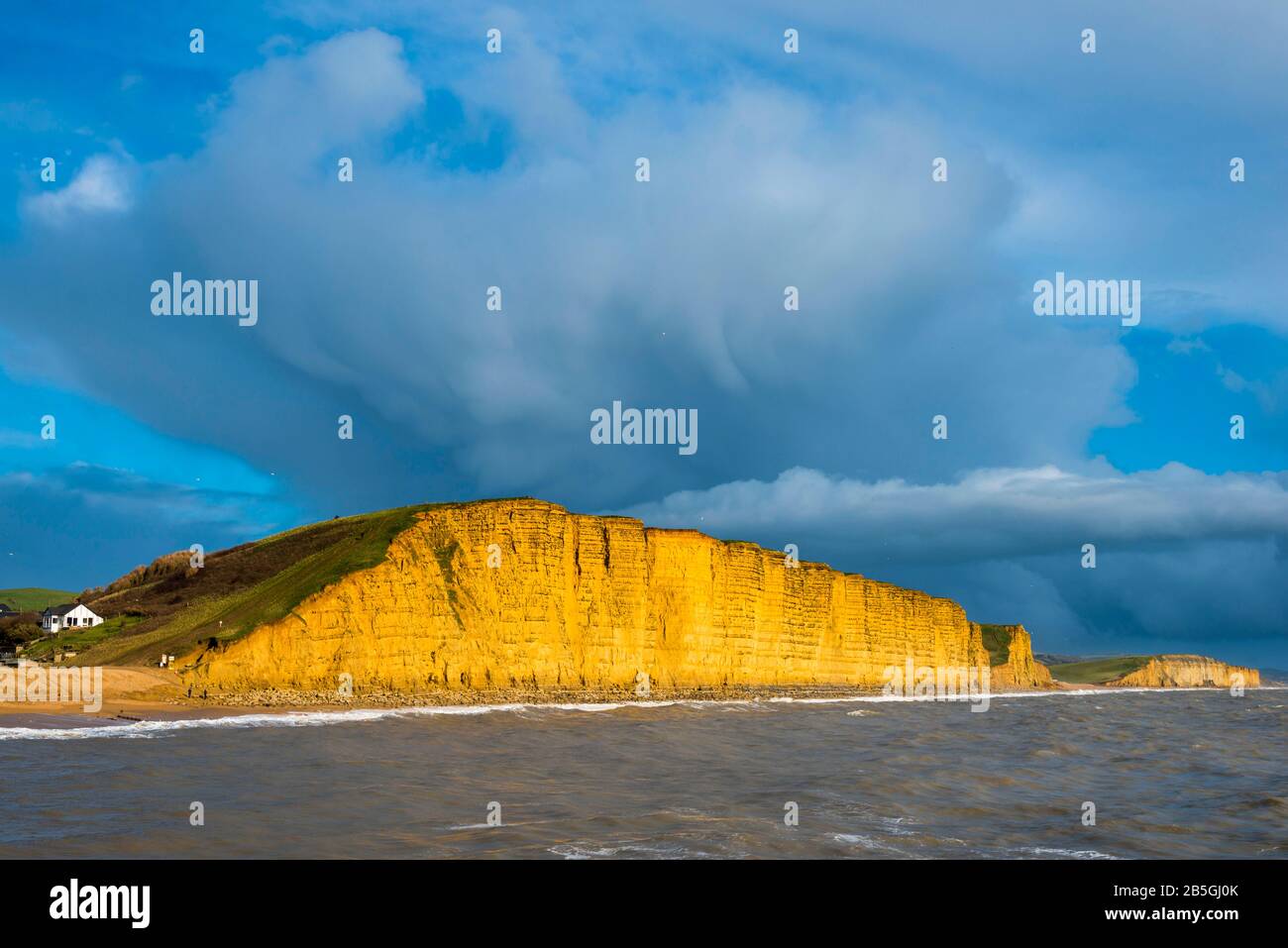 West Bay, Dorset, Großbritannien. März 2020. Wetter in Großbritannien. Dunkle Duschwolken passieren die Klippen, die am späten Nachmittag bei der Sonne in der West Bay in Dorset beleuchtet werden. Bildnachweis: Graham Hunt/Alamy Live News Stockfoto