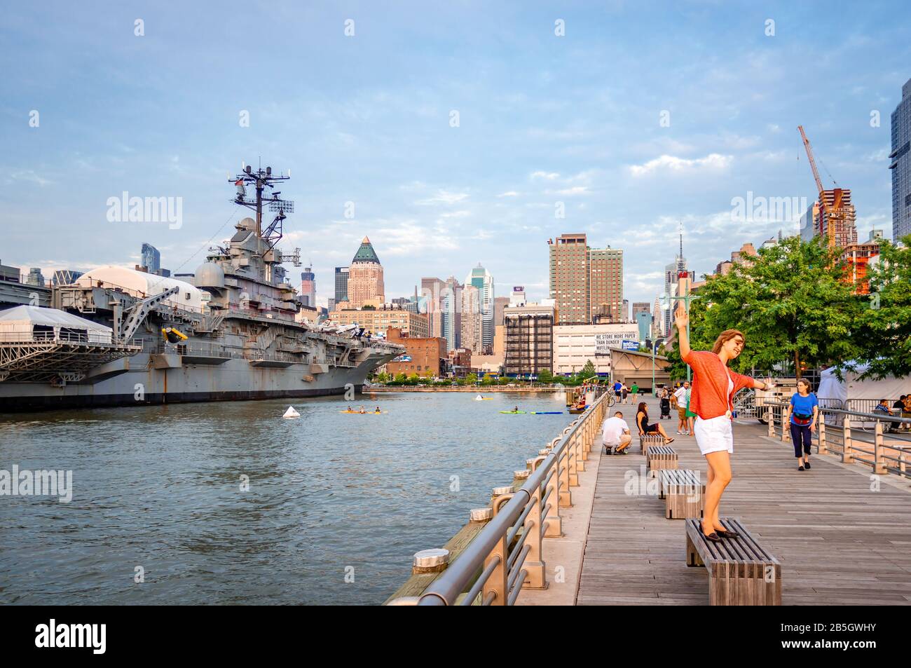 Die Leute genießen einen warmen Sommerabend am Pier 84 Dock. Die Skyline von Midtown Manhattan und die USS Intrepid (jetzt ein Museum) sind im Hintergrund. Stockfoto