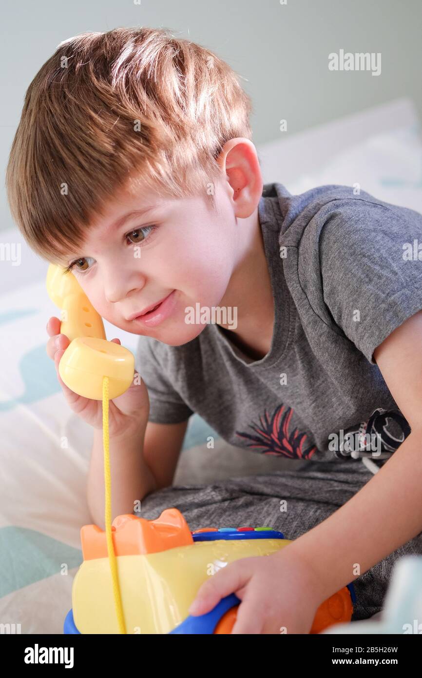 Kleiner Junge im Alter von 3 Jahren, der auf einem gelben Telefonspielzeug aus Kunststoff spielt Stockfoto