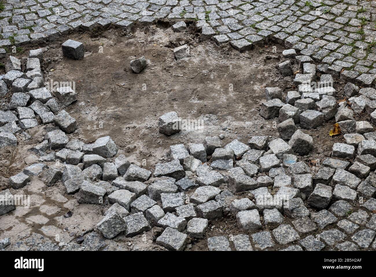 Steinsett Gehweg mit Loch und sichtbarem Boden, beschädigt und reparaturbedürftig Stockfoto