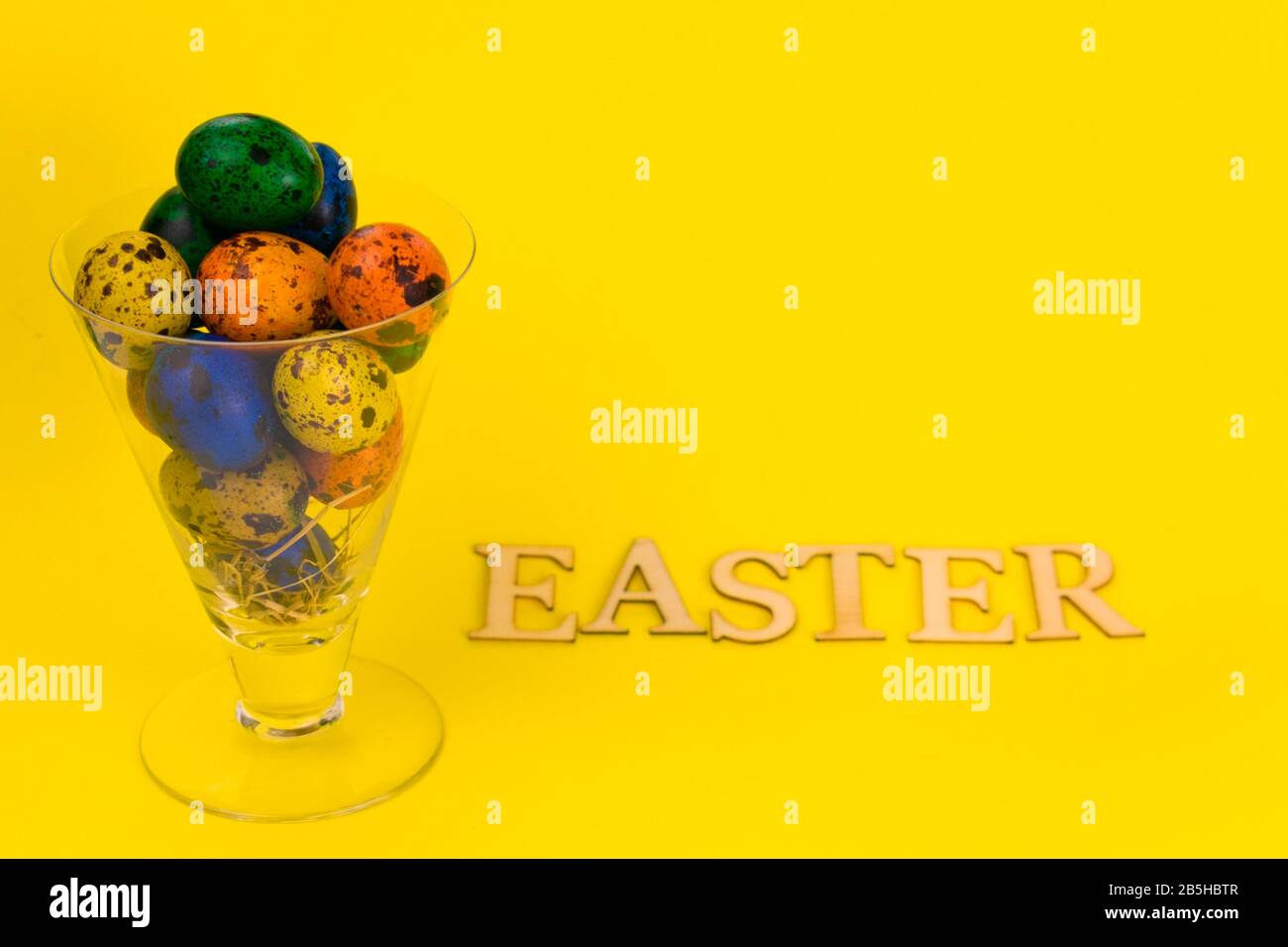 Mehrfarbige Ostereier in einem Glasbecher und die Aufschrift Ostern auf gelbem Grund. Stockfoto