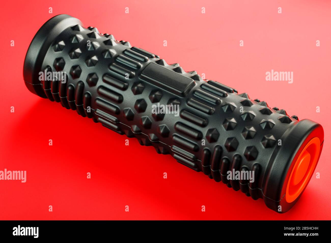 Schwarze, klumpige Schaummassagerolle, Körperrolle, Gummikugel auf rotem Hintergrund. Für die mechanischen und reflexartigen Effekte auf Gewebe und Organe. Stockfoto