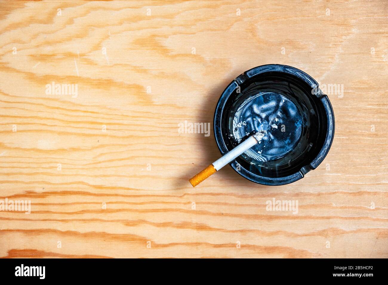Zigarette im Aschenbecher auf Holztisch, Suchtkonzept, Overhead-Ansicht Stockfoto