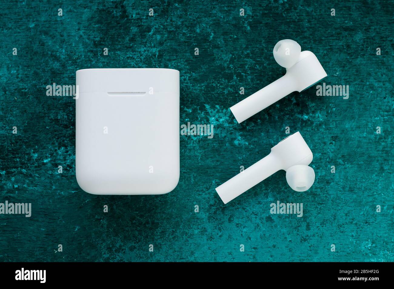 Kabellose bluetooth ® -Kopfhörer mit Ladeschale auf grün lackiertem Grunge. Gadget zum Musikhören. Elektronisches Gerät Stockfoto