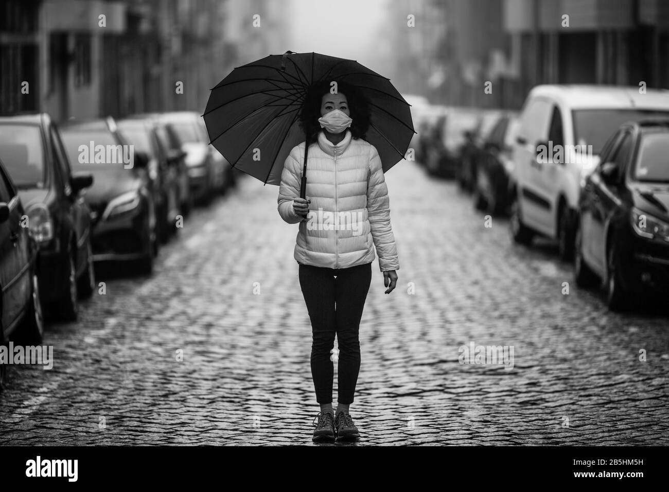Asian Woman in antiviraler Maske steht inmitten einer menschenleeren Straße in Foggy. Schwarzweißfoto. Stockfoto