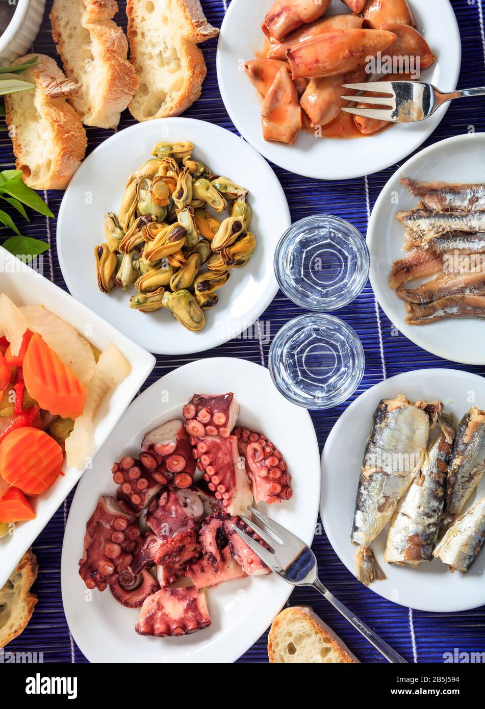 Kaltes Ouzo, Raki-Alkohol mit Meeresfrüchte-Meze auf weißen Gerichten. Zwei Gläser und verschiedene gesunde Weichtiere Hintergrund. Draufsicht, vertikal. Stockfoto