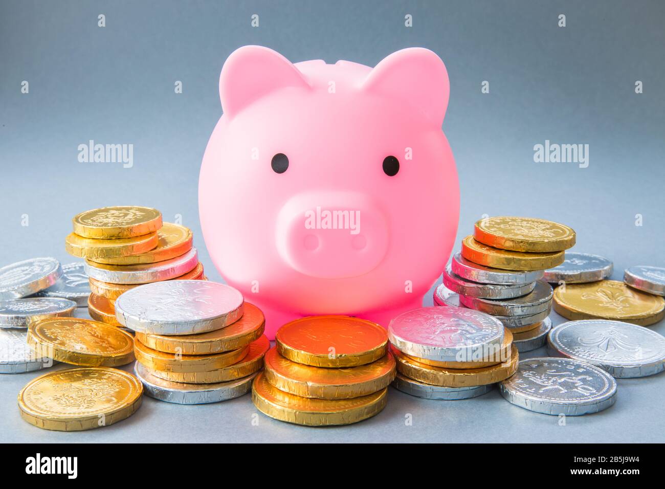 Ein Konzeptbild einer großen pinkfarbenen Schweinebank, umgeben von Bargeld, Münzen und Geld, die Ersparnisse, Bankgeschäfte und Unterricht für Kinder darstellen, um für ihr Geld zu sparen Stockfoto