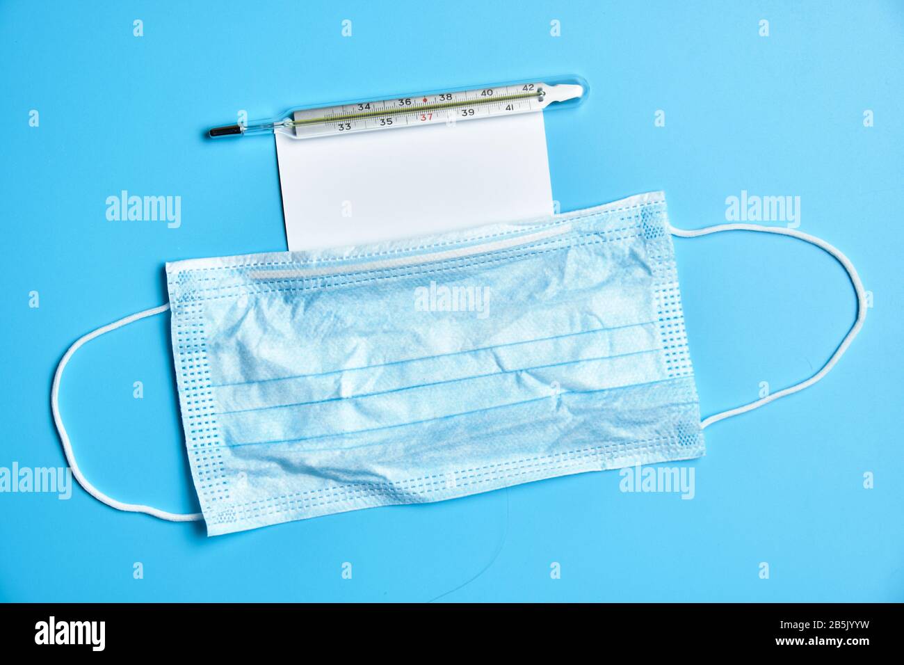 Medizinische Gesichtsmaske. Thermometer und weiße Karte auf blauem Hintergrund. Draufsicht. Stockfoto