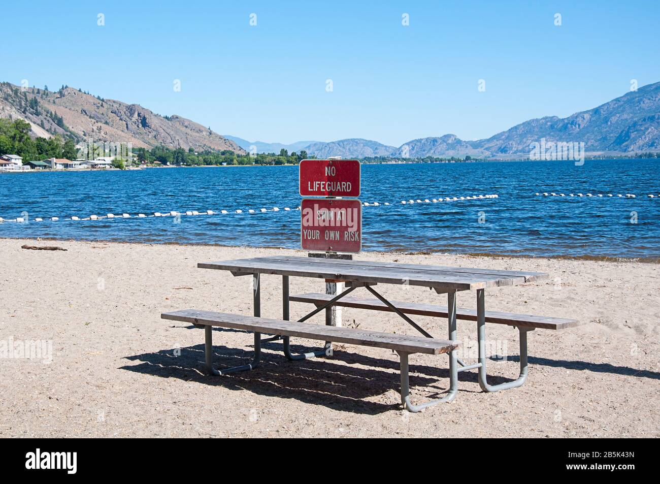 Lake Osoyoos State Park Strand kein Rettungszeichen, schwimmen Sie auf eigene Gefahr. In Oroville, Washington, gelegen, diese Landschaft mit einer Picknickbank. Stockfoto