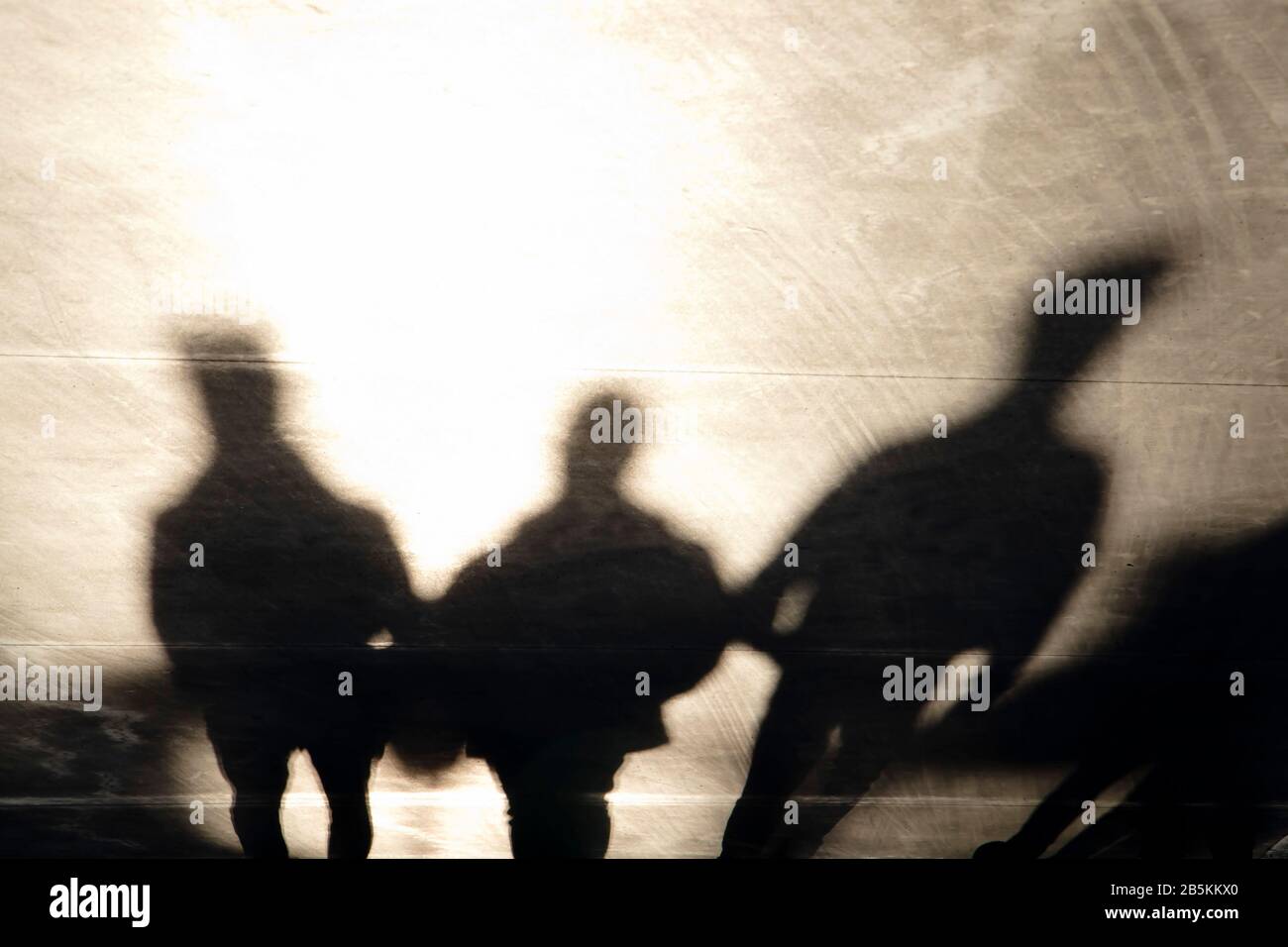 Schatten Silhouetten von drei mysteriösen Männern, die auf der Promenade bei Sonnenuntergang in Sepia schwarz und weiß laufen Stockfoto