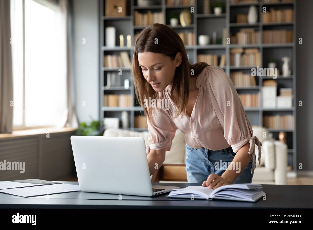 Angenehme junge Frau, die am Laptop arbeitet und am Tisch steht. Stockfoto