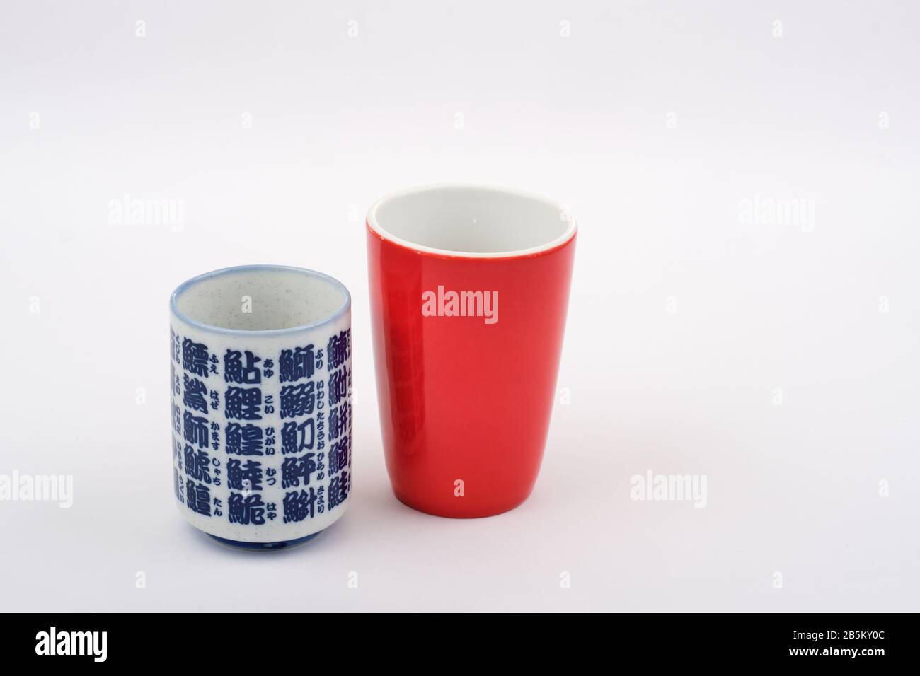 Reisekonzept East meets West mit rotem, traditionellem westlichem Teekaffee-Becher und blau-weißer japanischer Teekasse mit japanischer Schrift Stockfoto