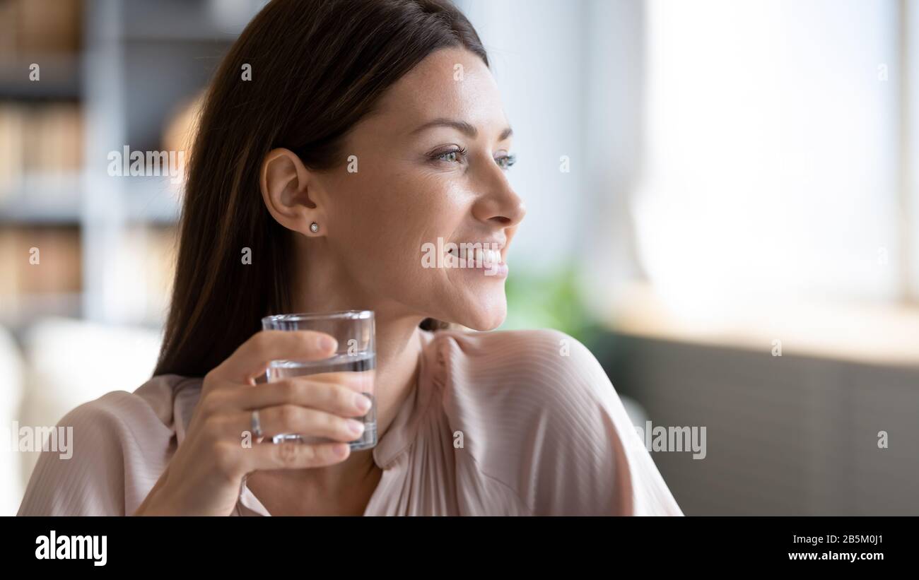 Junge verträumte Frau, die Glas frisches reines Wasser hält. Stockfoto