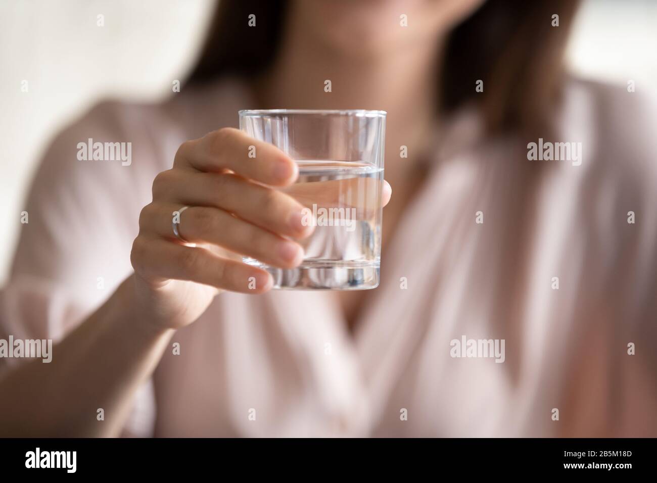 Junge Frau, die mit einem Glas Wasser an die Kamera reicht. Stockfoto