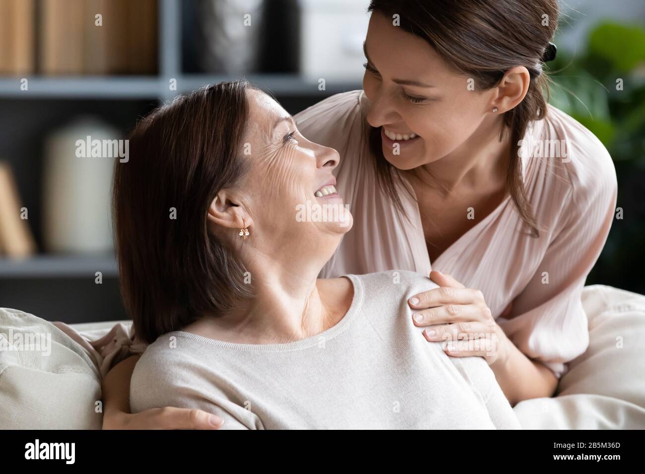 Glückliche ältere Frau, die auf lächelnde, attraktive Erwachsene Tochter blickt. Stockfoto